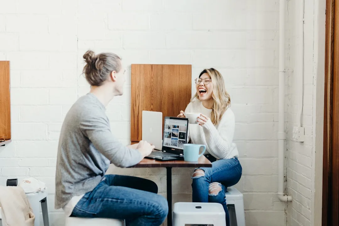 Two people chatting and laughing at a table with their laptops open